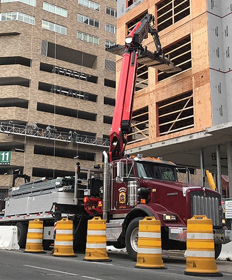 crane loading drywall into building under construction